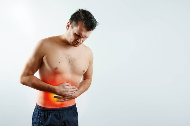 Front view, the man holds his hands to the stomach, abdominal pain, pain in the stomach highlighted in red. Light background. The concept of medicine, massage, physiotherapy, health. - Photo, image
