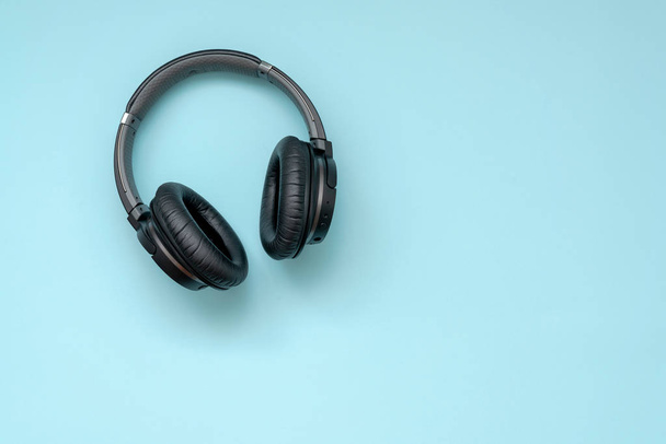 Μοντέρνο μαύρο ασύρματα ακουστικά σε μπλε φόντο. Η έννοια της μουσικής και της μόδας. - Φωτογραφία, εικόνα