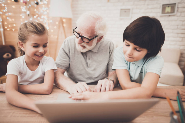 Grandpa and children sitting at table and using laptop - Photo, Image