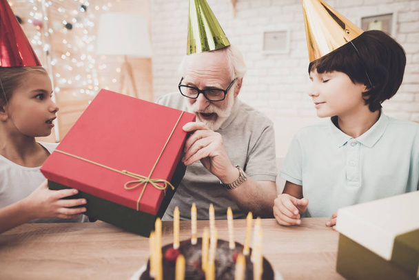 Grandfather, grandson and granddaughter on birthday party with presents and cake - Фото, изображение