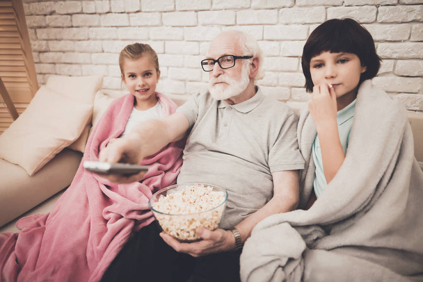 Abuelo y niños comiendo palomitas de maíz y viendo películas en la televisión
 - Foto, Imagen