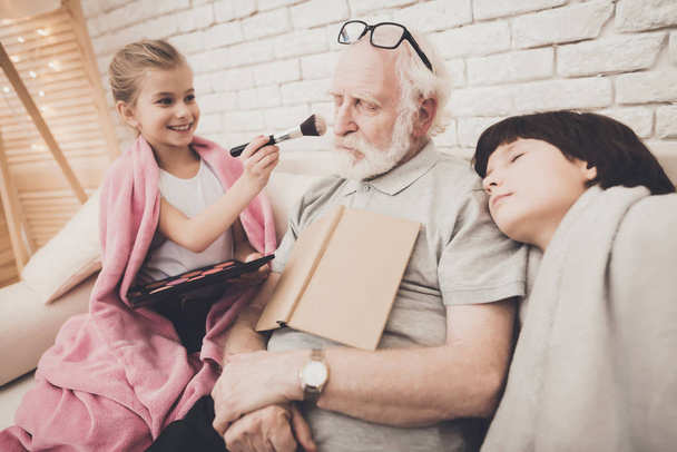 Girl painting face of grandfather, grandpa and boy sleeping - Foto, immagini