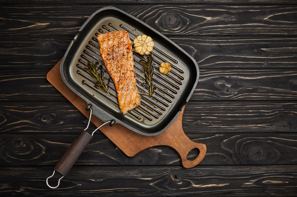 top view of arranged grilled salmon steak with rosemary on cutting board on black wooden tabletop - Fotografie, Obrázek