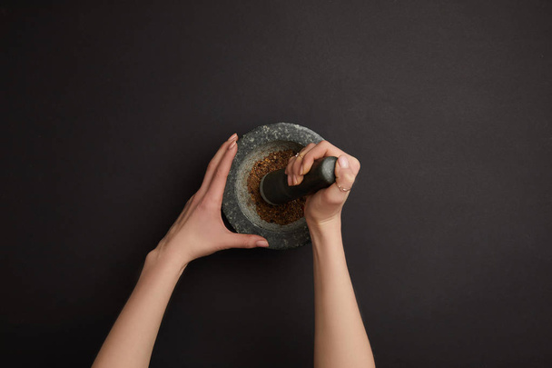 partial view of woman with mortar and pestle on black surface - Foto, Imagen