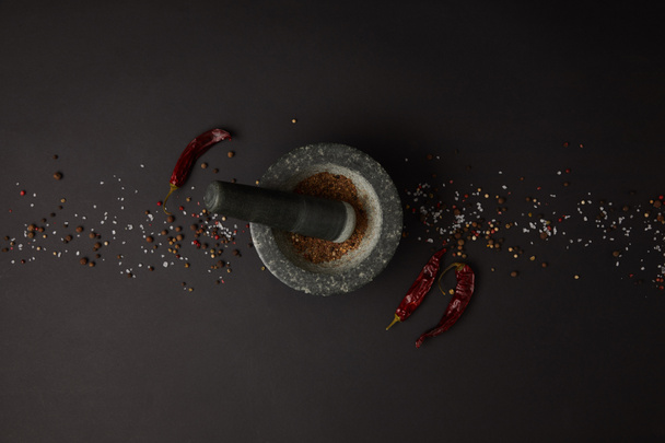 flat lay with mortar, pestle, spices and chili peppers on black tabletop - 写真・画像