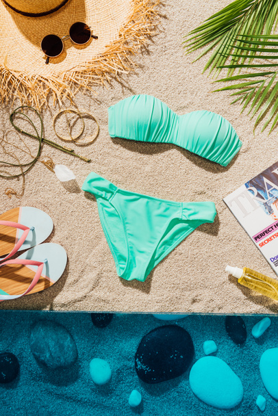 top view of stylish blue bikini with various accessories and magazine on sandy beach - Zdjęcie, obraz