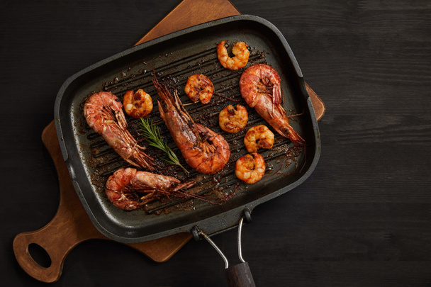 top view of grilled shrimps with rosemary on wooden cutting board on black tabletop - Valokuva, kuva