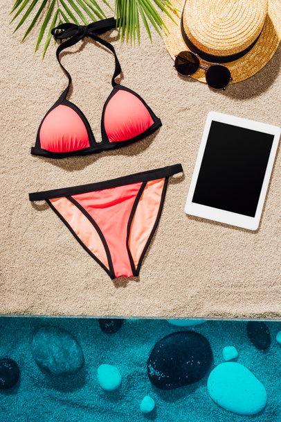 top view of stylish pink bikini with accessories and tablet on sandy beach - Foto, Bild