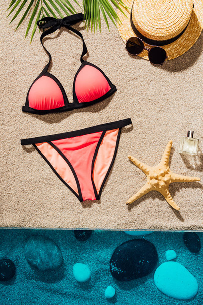 top view of stylish pink bikini with accessories and perfume on sandy beach - Zdjęcie, obraz