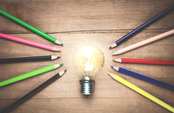 Light bulb with colorful pencils on the wood background. - Photo, Image