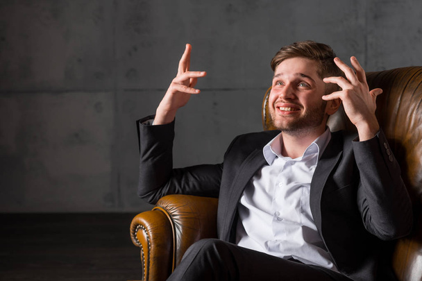Young businessman in suit gesticulating with hands sitting on sofa - Foto, imagen
