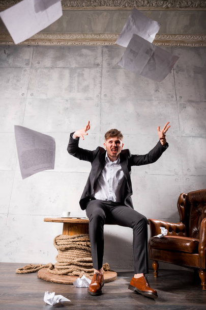 Jeune homme d'affaires en colère assis sur une table en bois et jetant des papiers
 - Photo, image