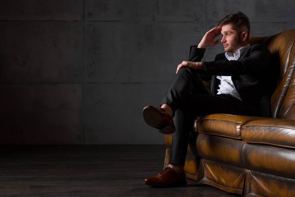 Young tired businessman in suit sitting on leather sofa - Fotoğraf, Görsel