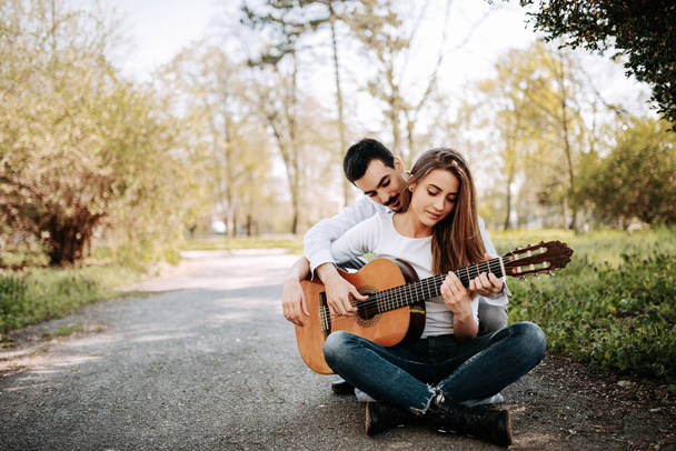 Young man teaching girlfriend playing guitar in park - Photo, image