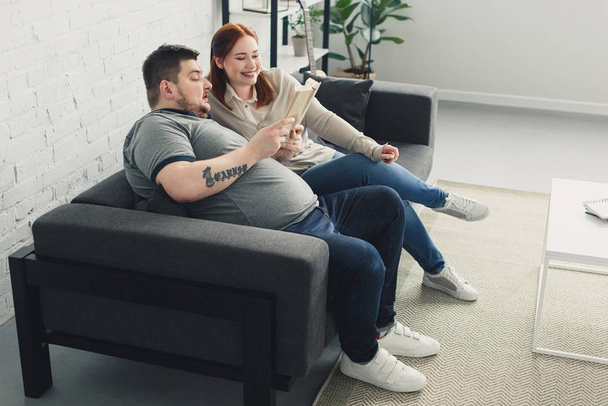 boyfriend and girlfriend reading book together on sofa at home - Fotoğraf, Görsel