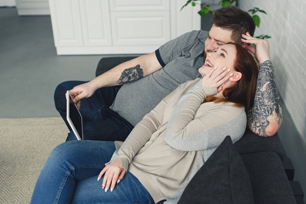riéndose novio y novia acostado en el sofá y viendo algo en la tableta en casa
 - Foto, Imagen