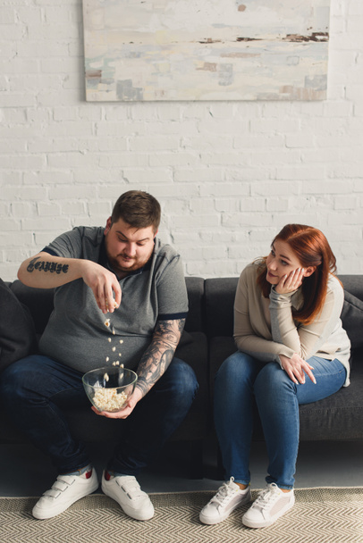 Girlfriend looking how overweight boyfriend playing with popcorn at home - 写真・画像