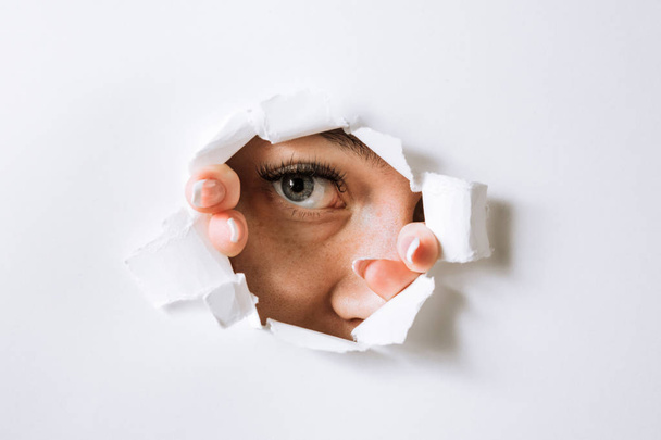 young woman peeks through a hole in a paper white wall - Photo, Image