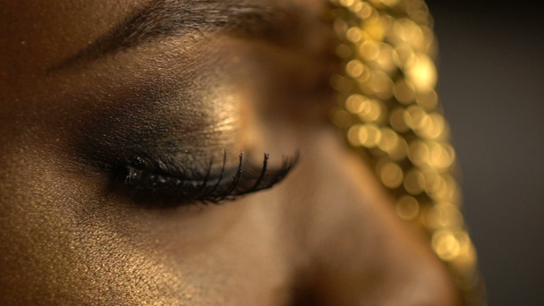 Open en gesloten ogen met bronzen eyeshadows en kat ogen op het gezicht van Afrikaanse meisje gouden juwelen draagt op haar hoofd. Close-up weergave. - Video