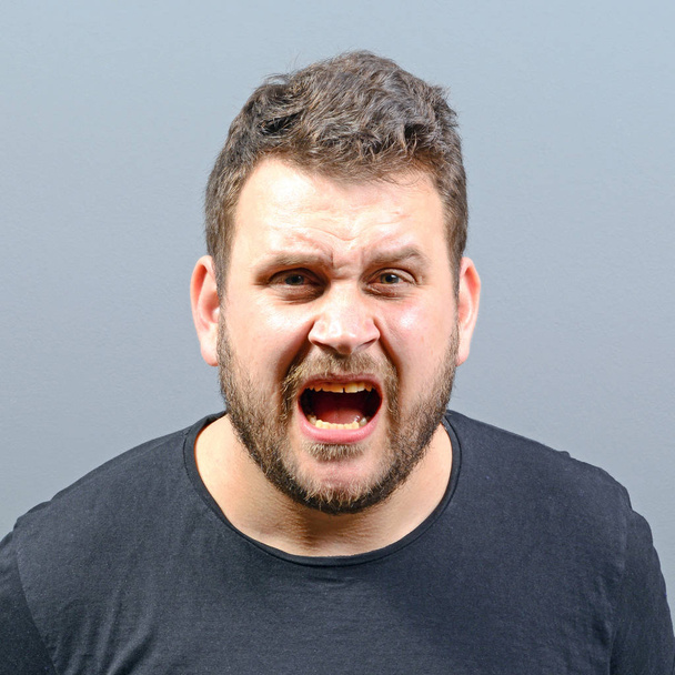 Muotokuva vihainen mies huutaa harmaata taustaa vasten
 - Valokuva, kuva