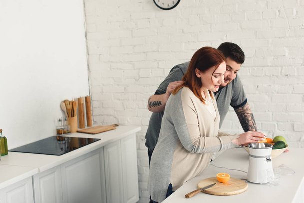 ylipainoinen poikaystävä halaus tyttöystävä, kun hän tekee mehua keittiössä
 - Valokuva, kuva