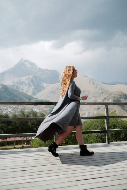 A girl is walking with a glass of wine on the terrace overlooking the mountains - Foto, Imagem