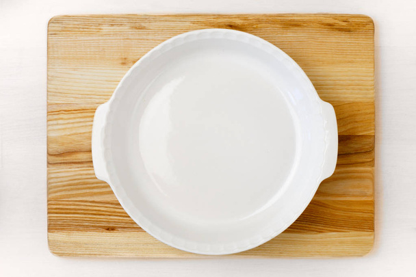 Teglia rotonda bianca vuota sul vassoio di legno che rimane sul tavolo di legno bianco
 - Foto, immagini