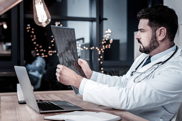 Концентрированный серьезный врач держит в руках рентгеновский снимок.
. - Фото, изображение