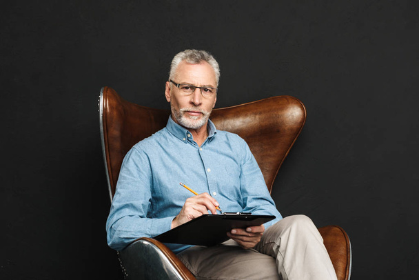 Portrait of middle aged man 60s with grey hair and beard sitting - Foto, afbeelding