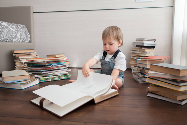 A cute baby sits on the floor and looks in a large book. - Photo, Image