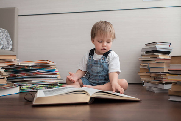 Un bebé lindo se sienta en el suelo y mira en un libro grande
. - Foto, Imagen