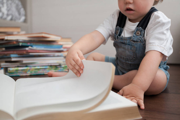 Een klein kind is bladeren door de pagina's van een groot boek. - Foto, afbeelding