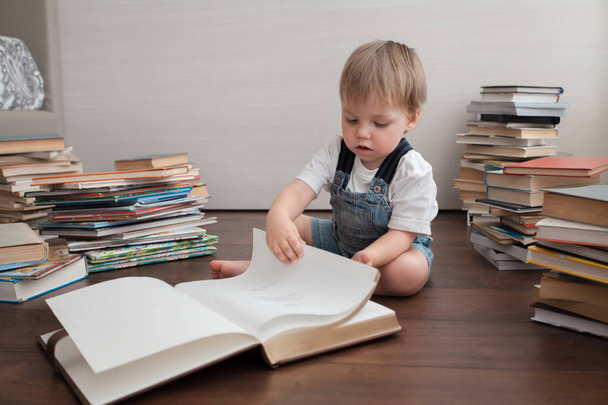 A cute baby sits on the floor and looks in a large book. - Фото, зображення