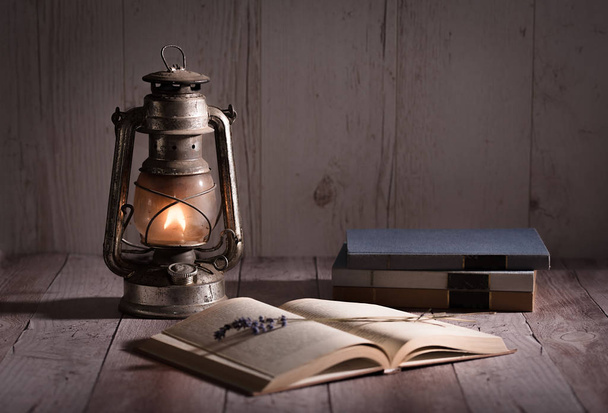 Old, antique book opened and burning kerosene lamp on wooden table - Fotoğraf, Görsel