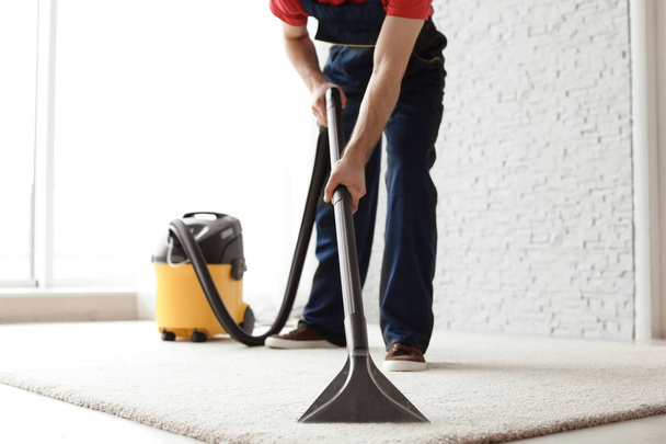 Male worker cleaning carpet with vacuum indoors - 写真・画像
