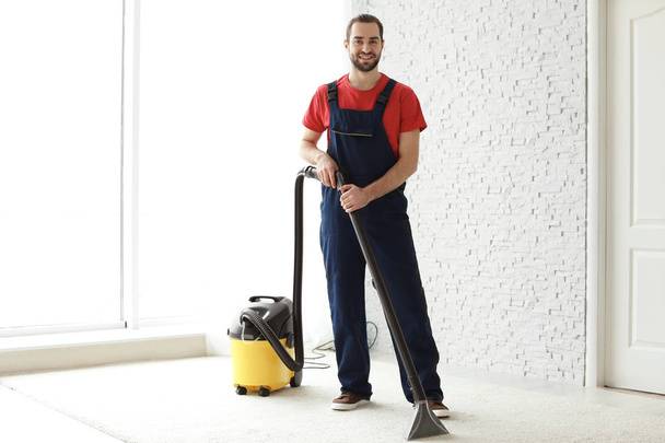 Male worker cleaning carpet with vacuum indoors - Fotografie, Obrázek