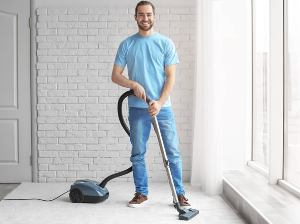 Young man cleaning carpet with vacuum at home - Photo, image