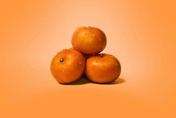 Спелый апельсин свежий и влажный мандарин, фрукты клементина, капли воды, на оранжевом фоне
 - Фото, изображение