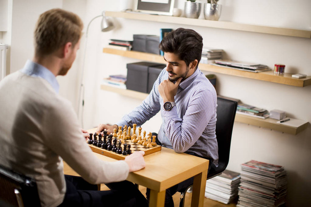 Two young men playing chess in room - Φωτογραφία, εικόνα
