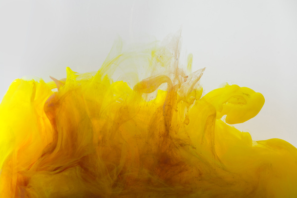 Vista de cerca de la mezcla de tintas amarillas y marrones salpicaduras en agua aislada en gris
 - Foto, imagen