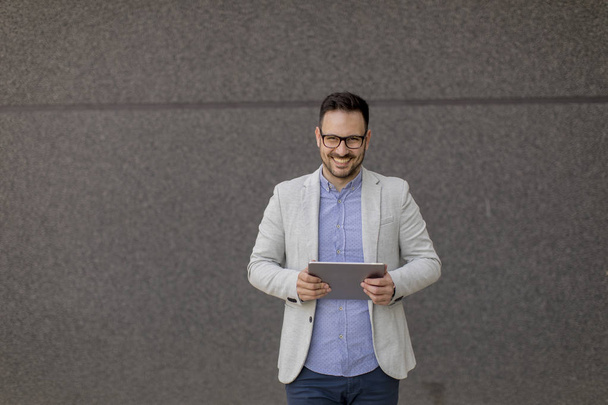 Knappe jonge zakenman met digitale tablet door de grijze muur - Foto, afbeelding