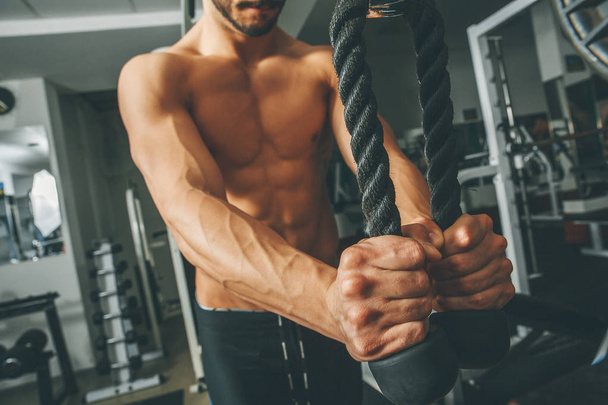 Torso desnudo hombre muscular haciendo ejercicio en el gimnasio haciendo ejercicios con cuerda de tríceps
 - Foto, imagen