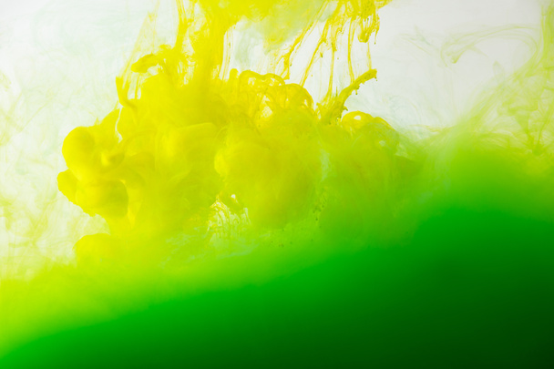 Vista de cerca de la mezcla de tintas verdes y amarillas salpicaduras en agua aislada en gris
 - Foto, Imagen