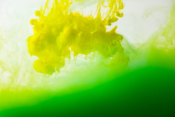 close up view of mixing of green and yellow paints splashes  in water isolated on gray - 写真・画像