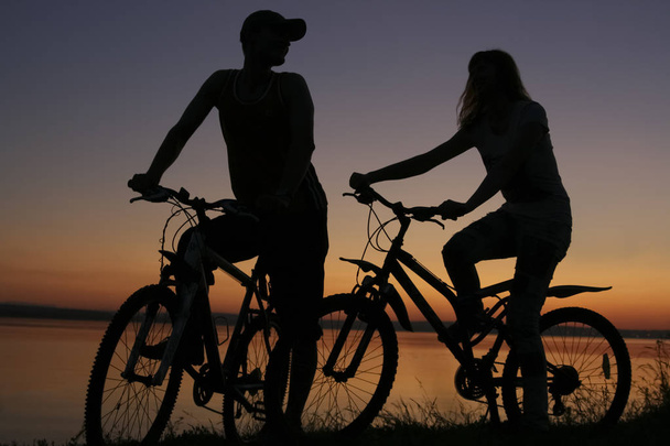  Sporty friends on bicycles on sunset. Silhouette of  couple along shoreline coast.  - Foto, imagen