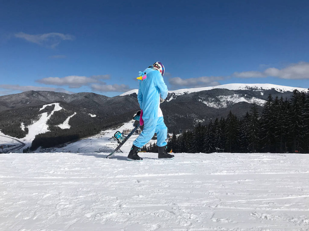 Дівчина в синьому, рожевому єдиноріг піжама Кігурумі на відкритому повітрі зі сноубордом на лижному звіті в снігових горах
. - Фото, зображення