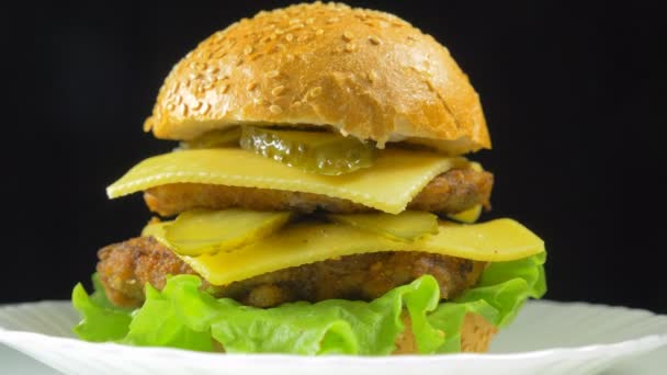 Velký hamburger s masem a sýrem se otočí na talíři - Záběry, video