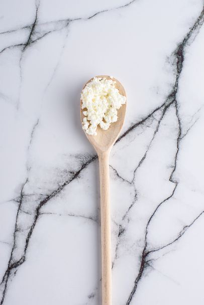 top view of wooden spoon with fresh cottage cheese on marble surface - Photo, Image