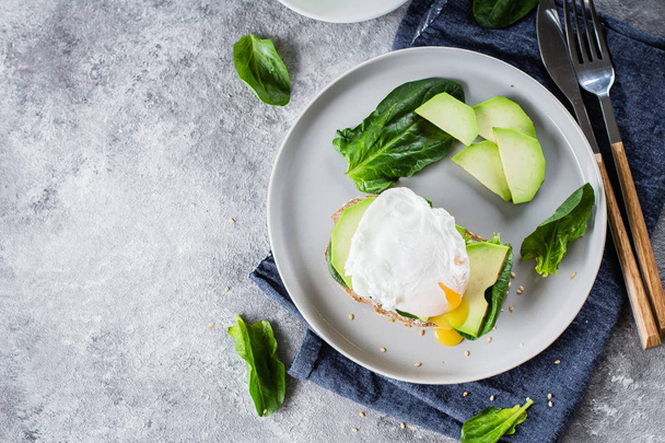 Sandwich with avocado, spinach and poached egg on whole wheat bread on plate on stone background - Photo, Image