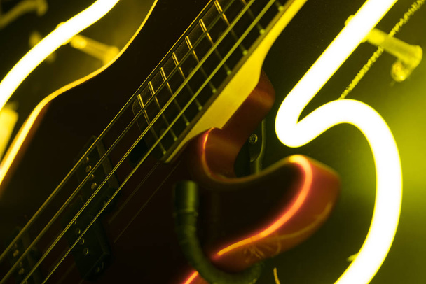 Bass guitar fretboard closeup, yellow neon lights, artistic background - Photo, image